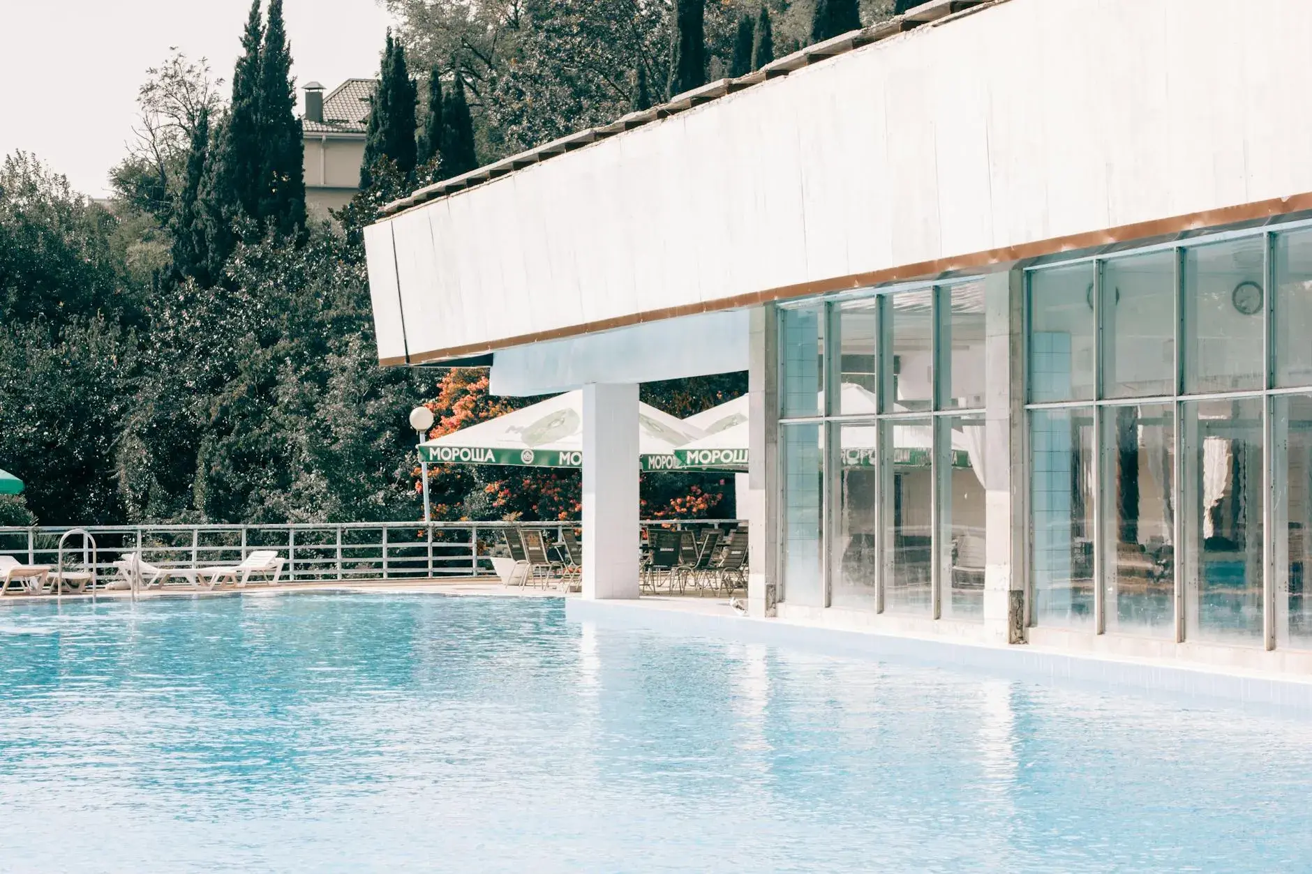 Et indbydende kig over en swimmingpool ved et moderne resort, hvor sollyset reflekteres smukt i de store glaspartier.