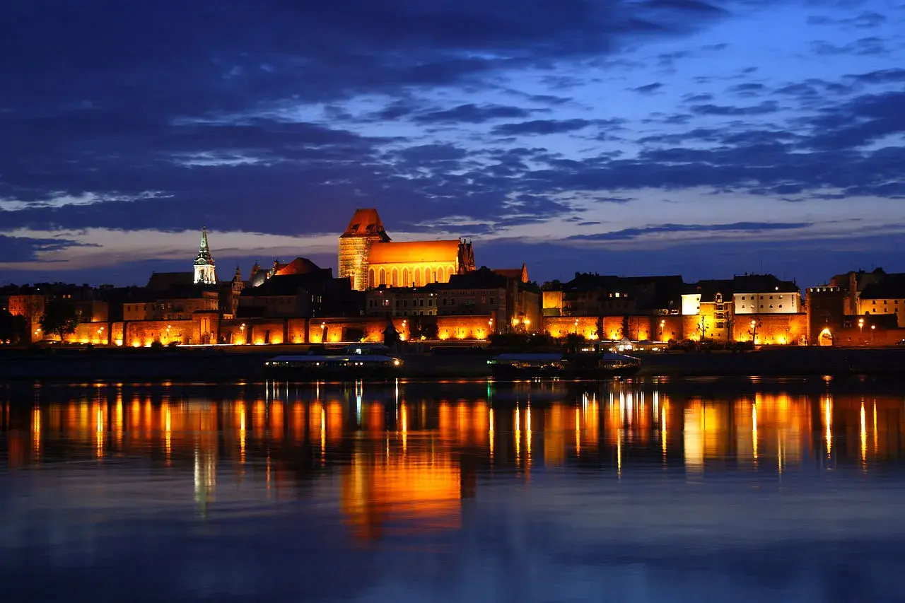 A captivating view of Toruń's medieval Old Town illuminated by night, reflecting on the Vistula River.