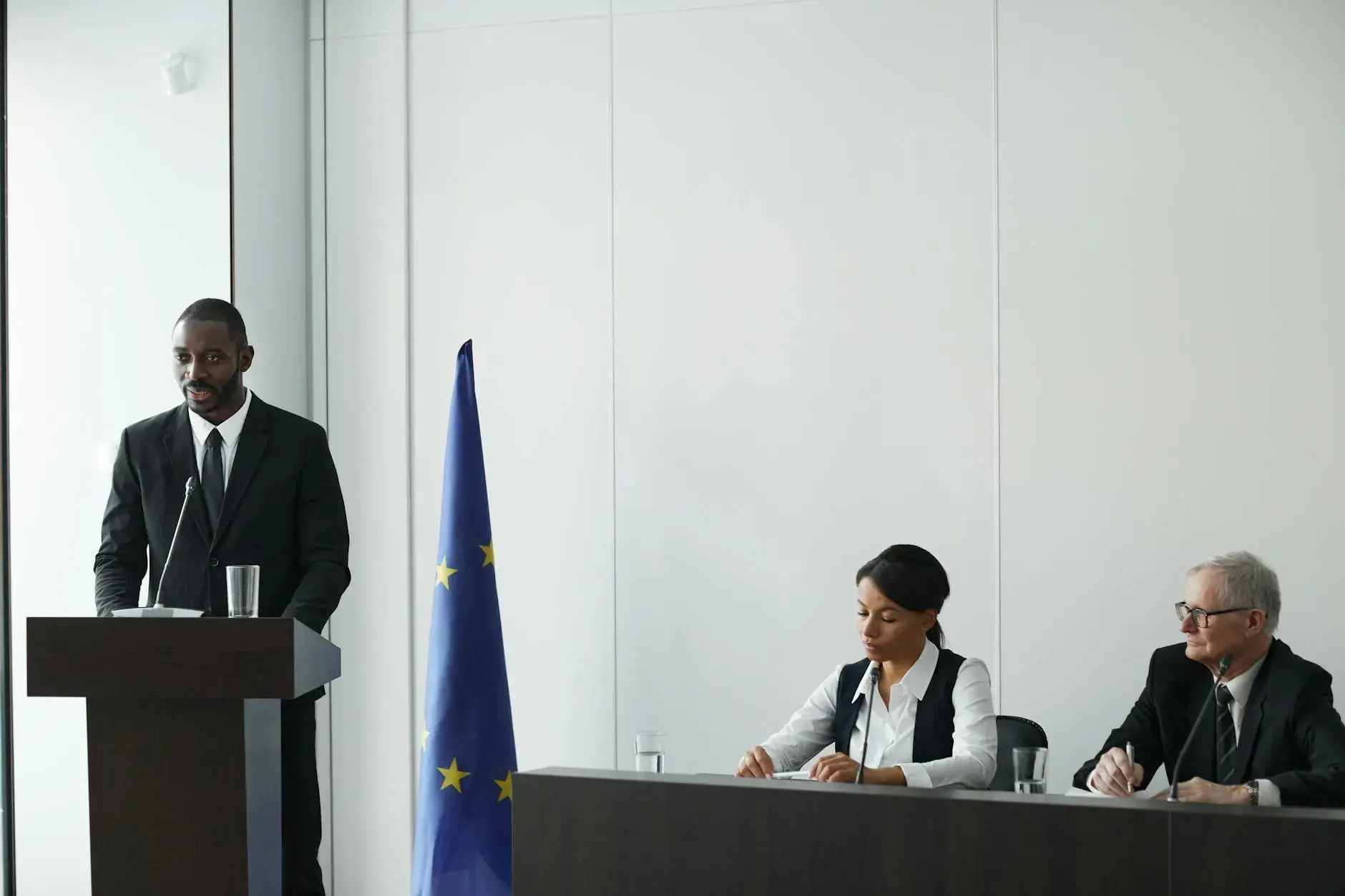En professionel konference med forskellige talere i jakkesæt, hvor der diskuteres internationalt diplomati. EU-flaget er synligt i baggrunden.