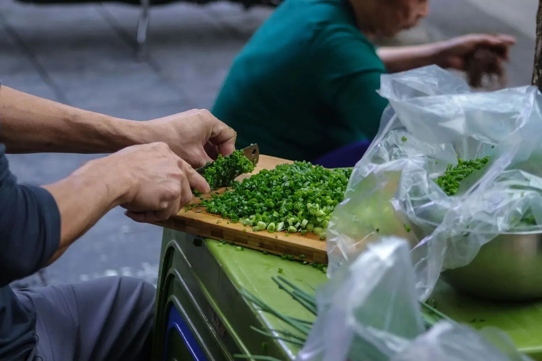 A close-up shot of hands skillfully chopping fresh spring onions on a wooden cutting board.