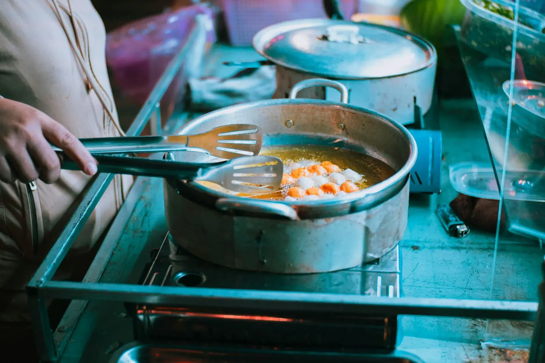 A close-up shot of someone flipping food in a pan using tongs, capturing the heat and movement of indoor cooking.