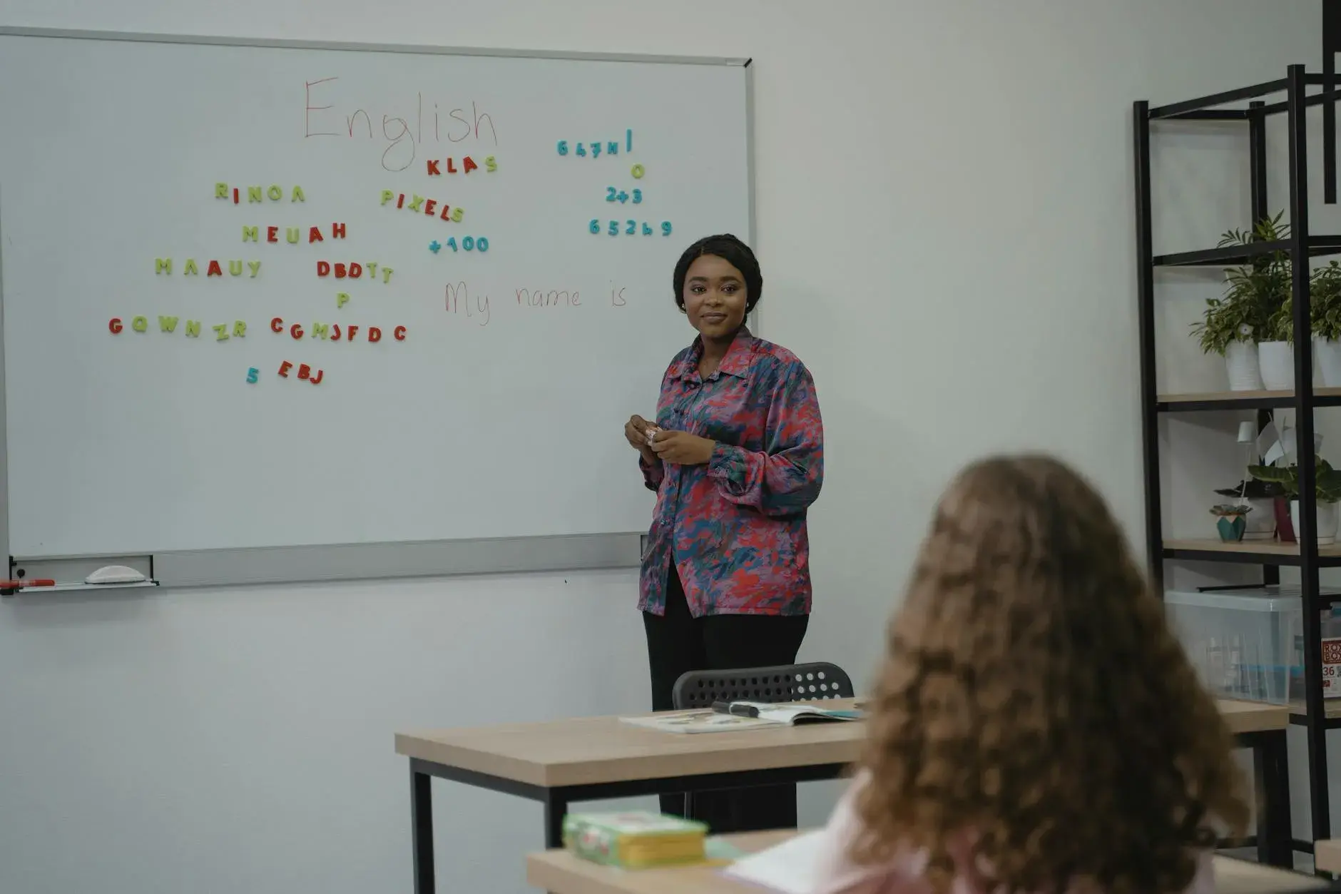 A teacher uses a whiteboard to explain English grammar concepts to a student in a classroom.
