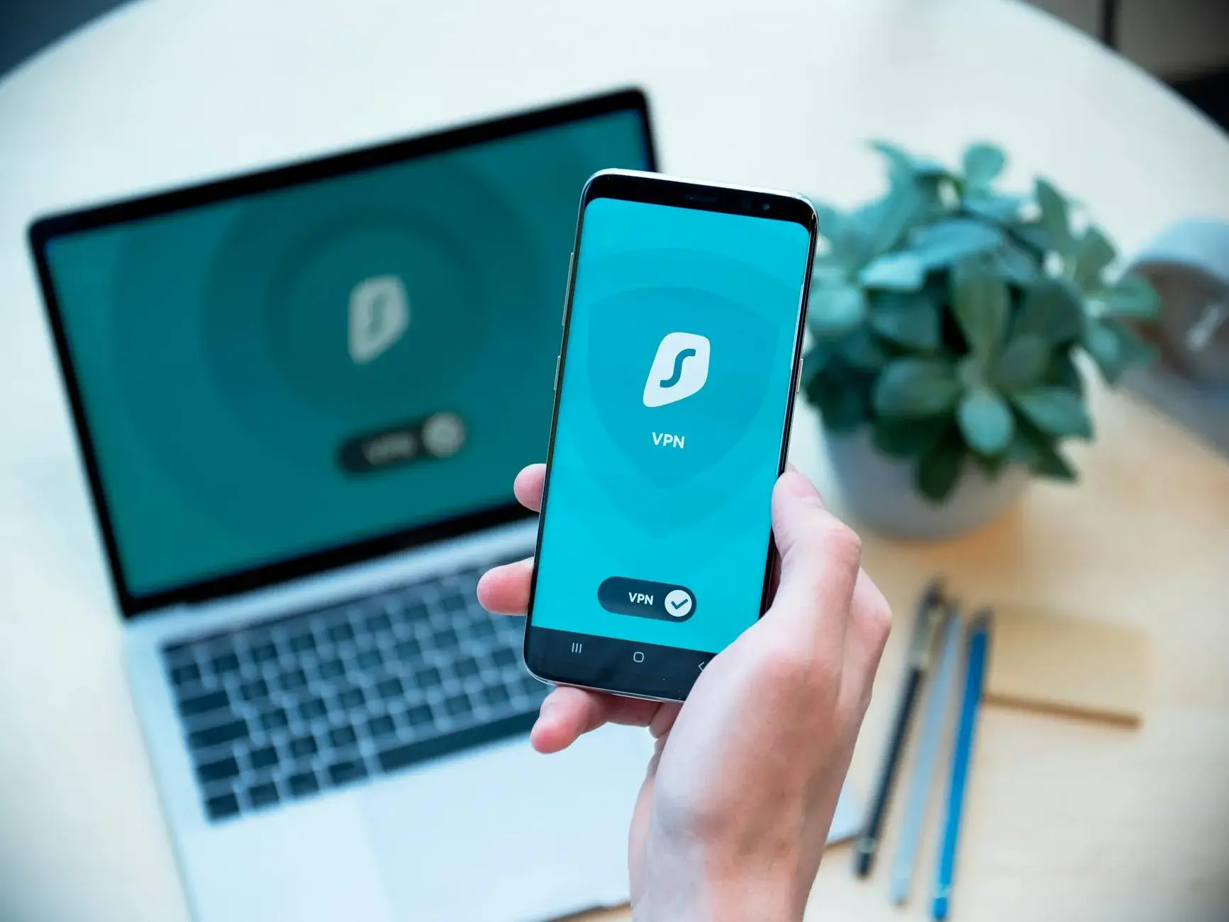 En hånd holder en smartphone med en VPN-app, mens en laptop står i baggrunden. Billedet illustrerer digital sikkerhed og privatliv online.