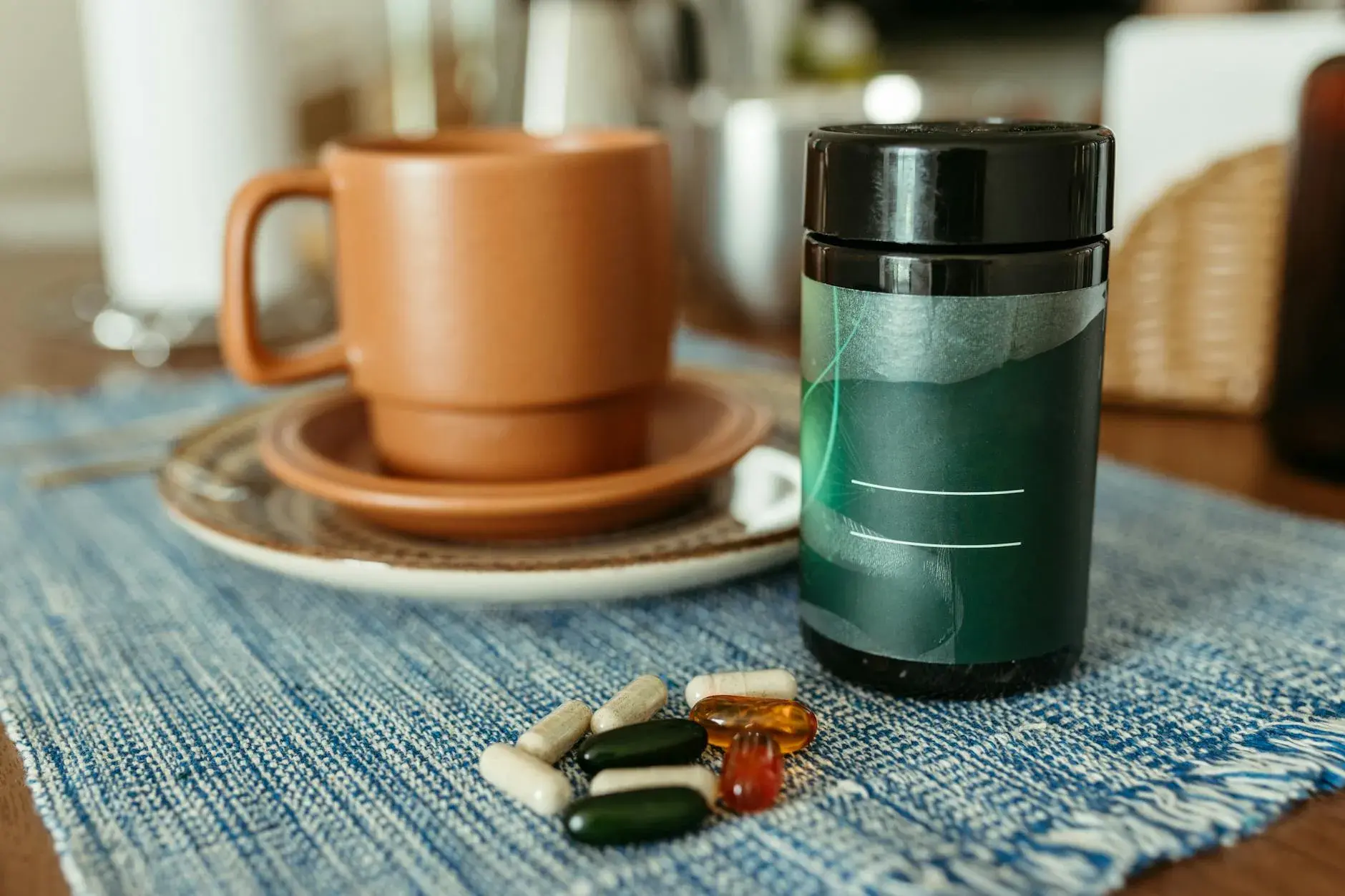 En række kapsler ligger ved et keramisk krus og en beholder på et bord. Billedet illustrerer daglig medicin og sundhed i hjemmet.