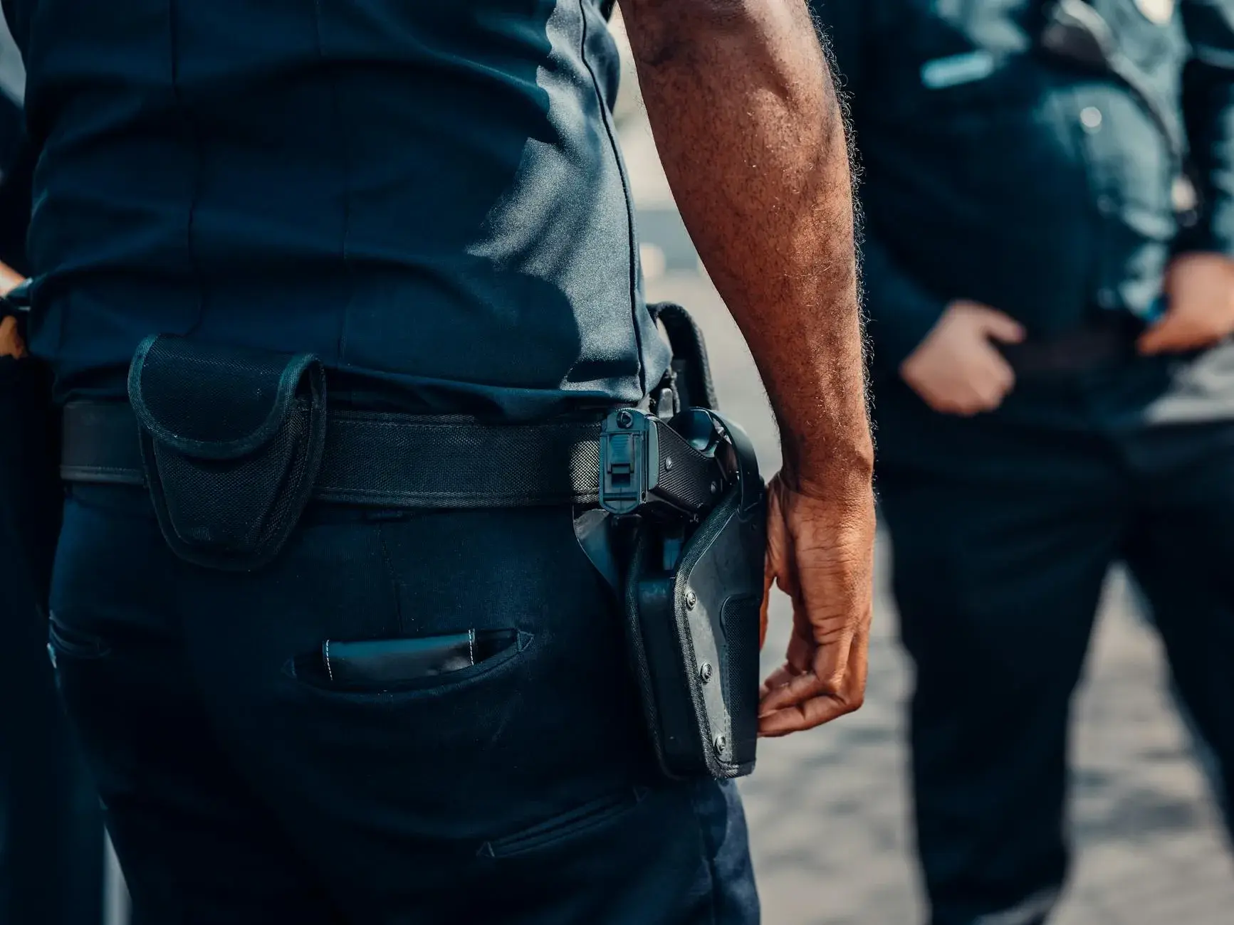 Close-up af en politibetjents pistol, der sidder sikkert i hylsteret ved hoften. Billedet signalerer professionalisme og beredskab.