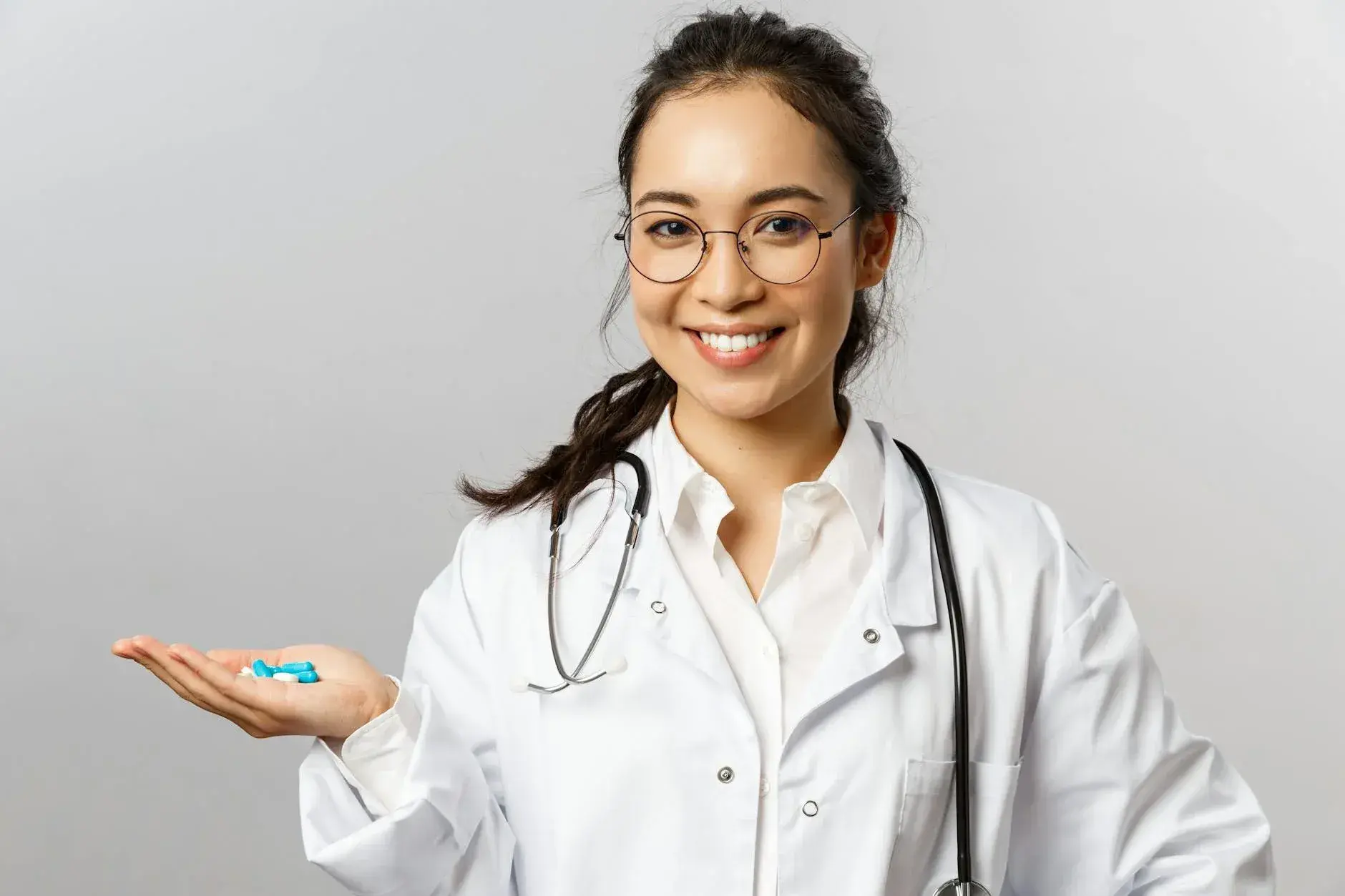 En kvindelig læge smiler og holder piller, mens hun formidler tryghed og behandling. Billedet understøtter temaer som sundhed, medicin og patientomsorg.