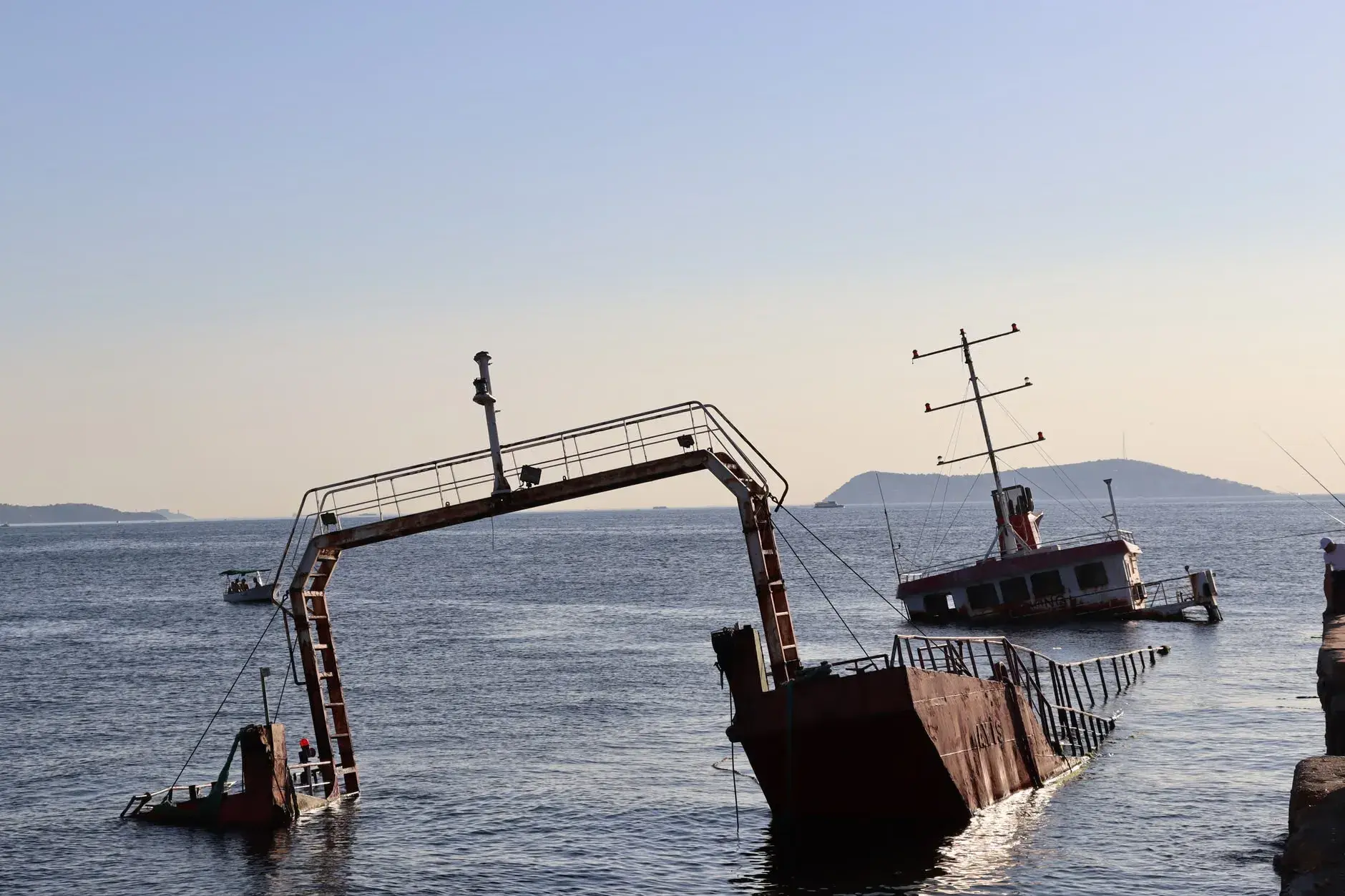 Et forladt skibsvrag delvist nedsænket i havet ved solnedgang, skabende en dramatisk havudsigt. Billedet viser en stille og øde scene.