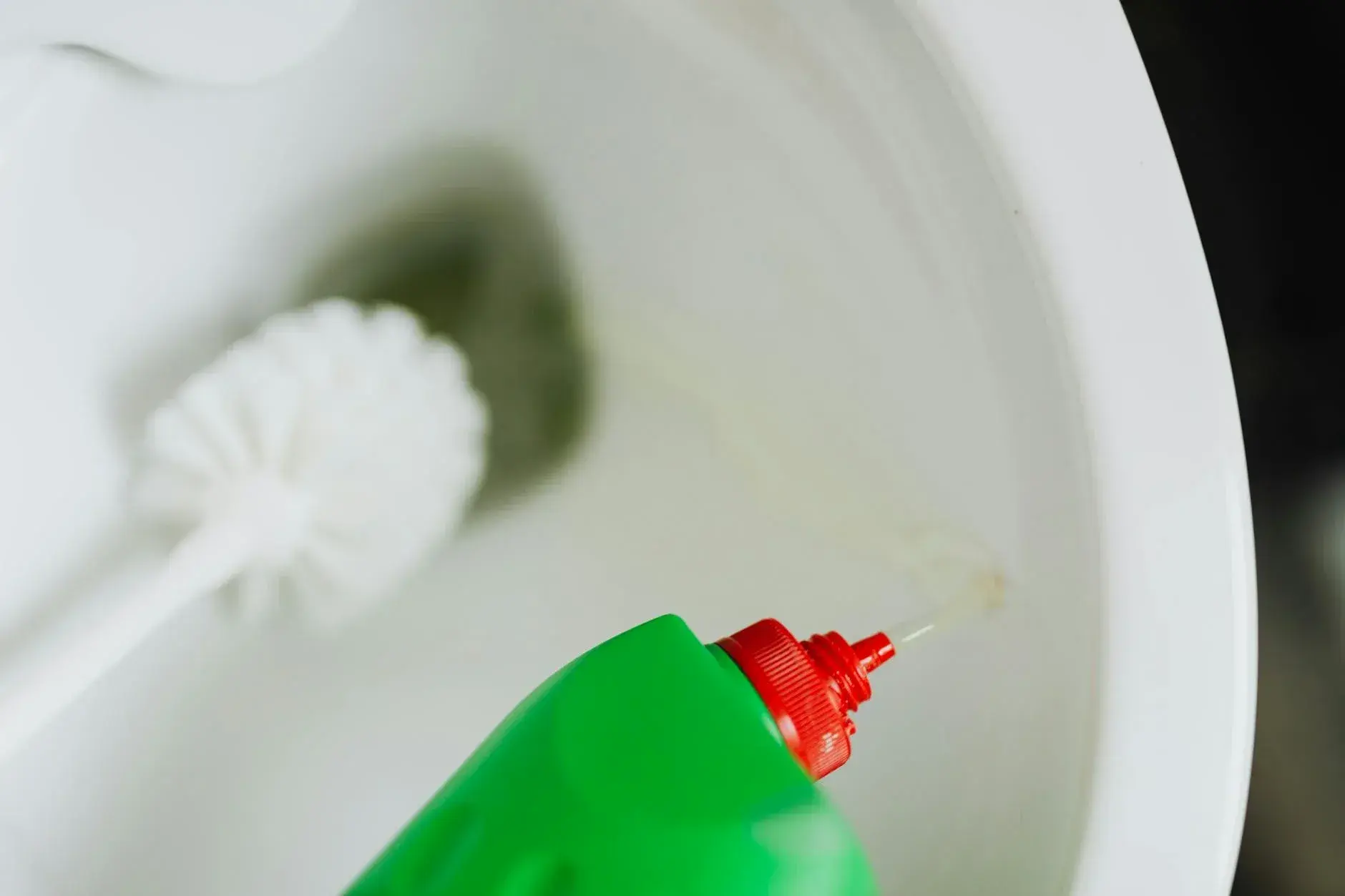 En grøn flaske med rengøringsmiddel hældes i toiletkummen for at sikre optimal hygiejne på badeværelset.