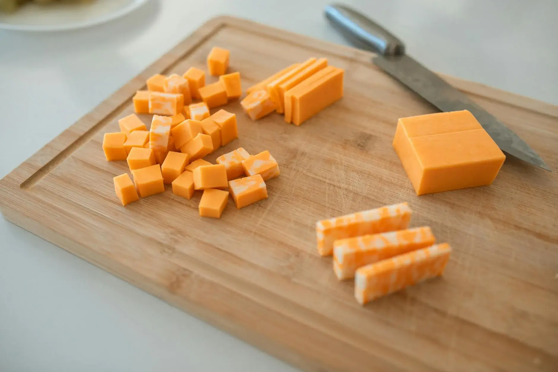 Nærbillede af skiver af cheddar og colby-jack på et træskærebræt med en kniv i billedet. Perfekt til mad- og oste-relateret indhold.
