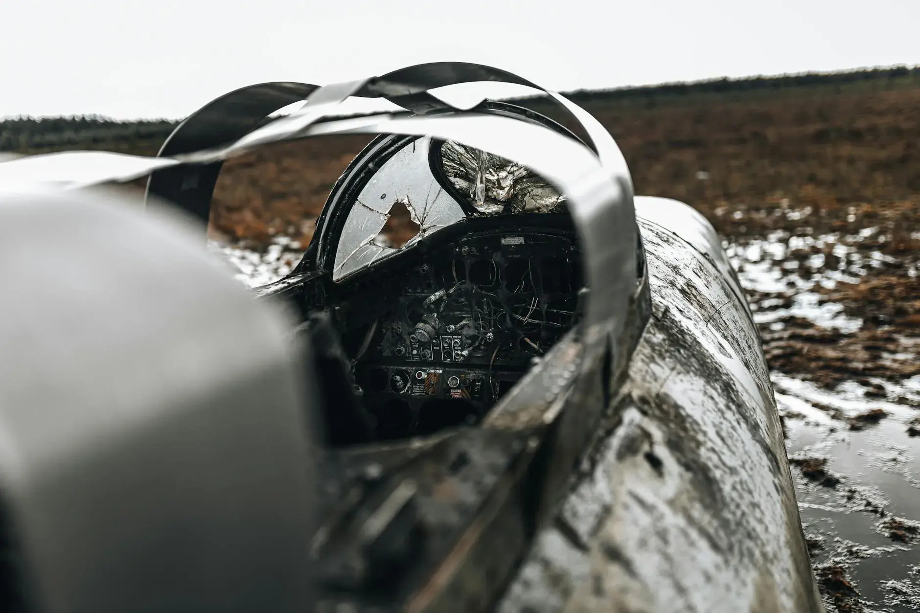 A desolate field with the remnants of a military aircraft cockpit following a crash, highlighting the aftermath of a tragic incident.