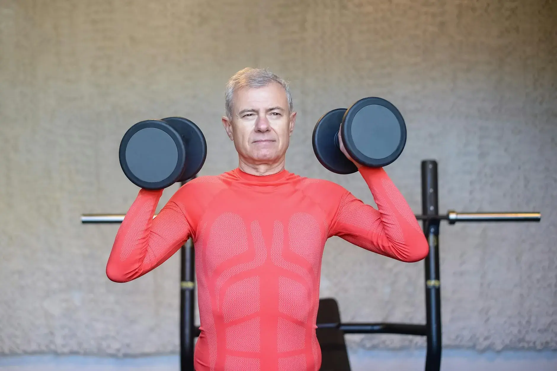 A senior man in a vibrant red outfit demonstrates strength training indoors, promoting an active lifestyle.