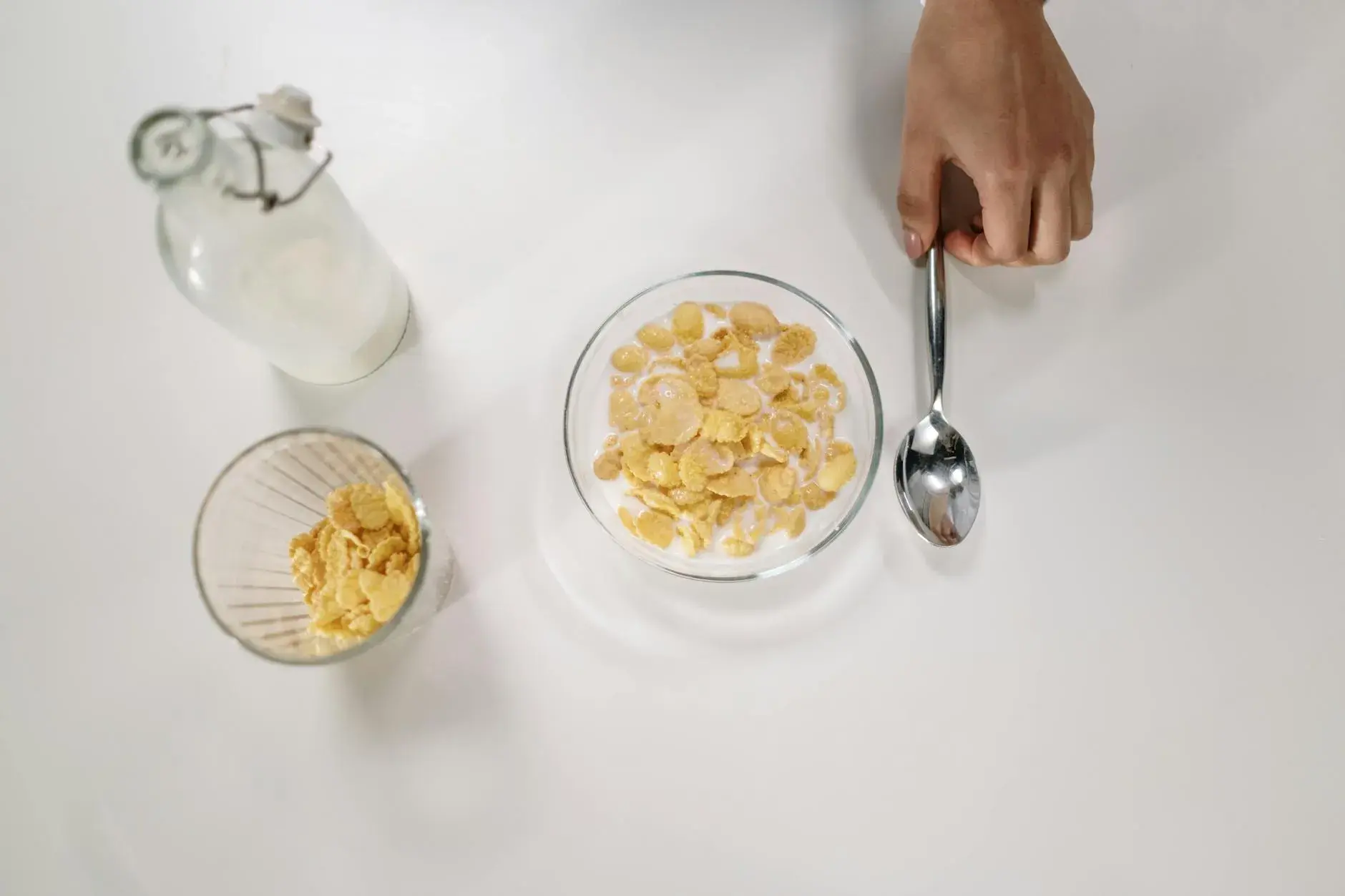 Et top-down billede af en skål med cereal, mælk og en ske på en ren, hvid overflade. En mælkeflaske står ved siden af og understreger temaet om morgenmad.