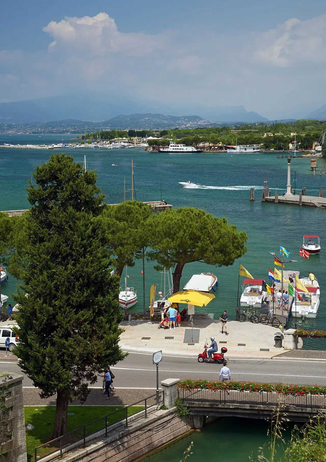 Panoramisk udsigt over Gardasøen set fra Peschiera del Garda i Italien. Landskabet og vandfladen skaber en rolig, naturskøn stemning.