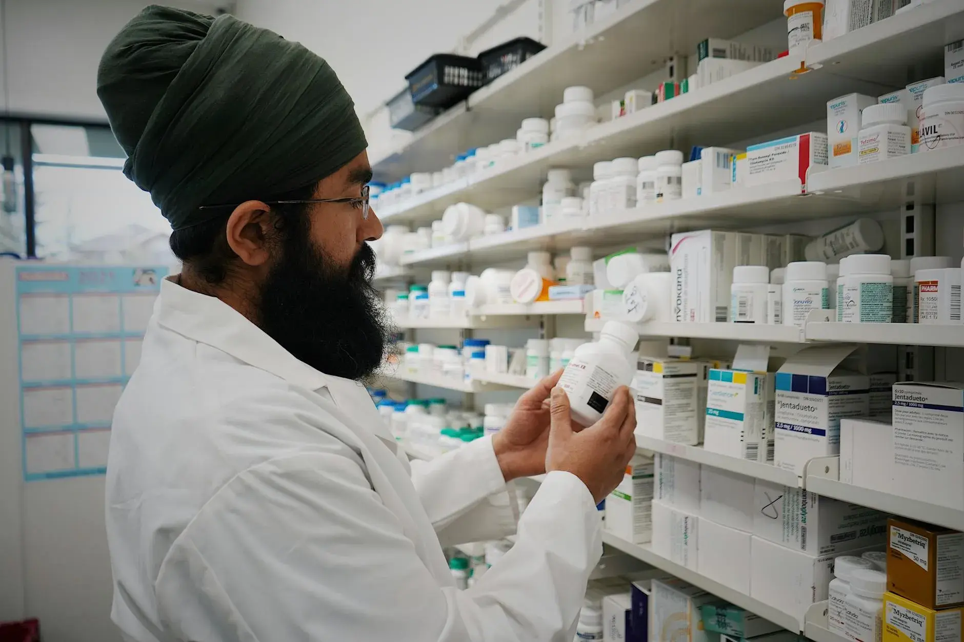 En farmaceut med turban organiserer hylder i et apotek. Billedet formidler fokus på sundhed og rådgivning.