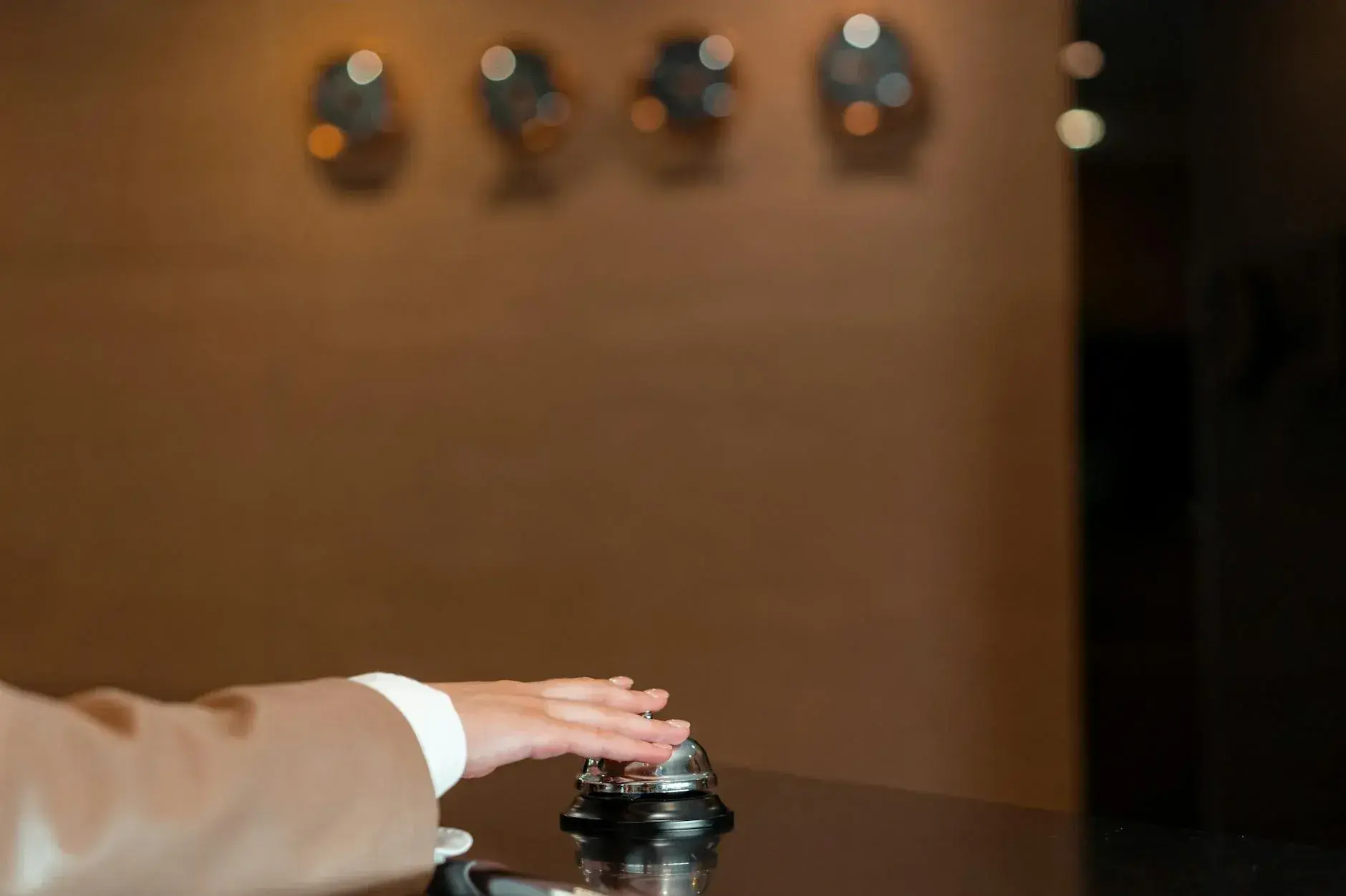 En hånd trykker på en klokke ved hotellets reception. Billedet symboliserer service, gæstfrihed og hurtig assistance.
