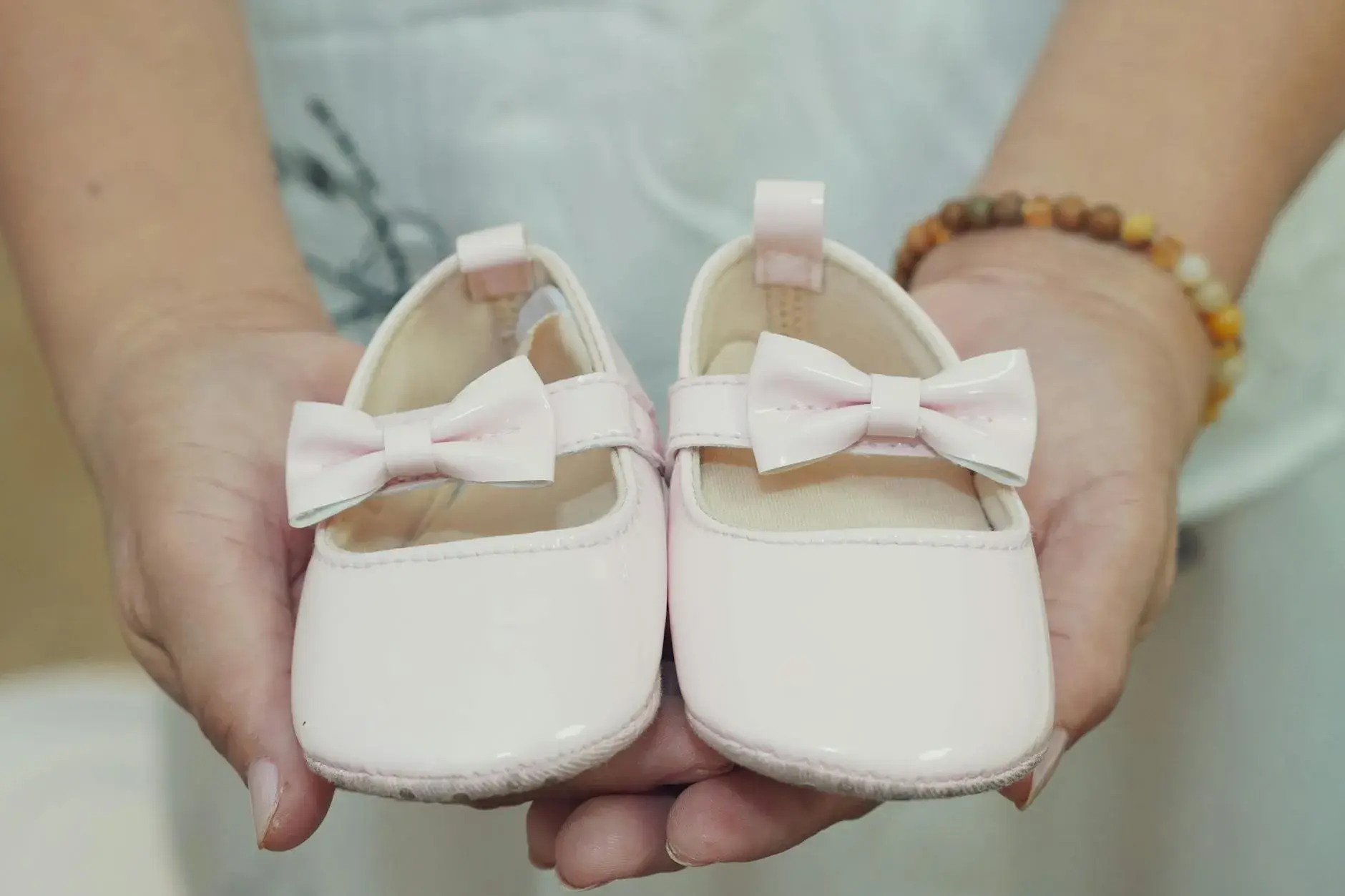 Et par små babysko med sløjfer holdes i hænderne, perfekt til en baby-girl annoncering eller gaveidé. Stemningen er varm og kærlig.