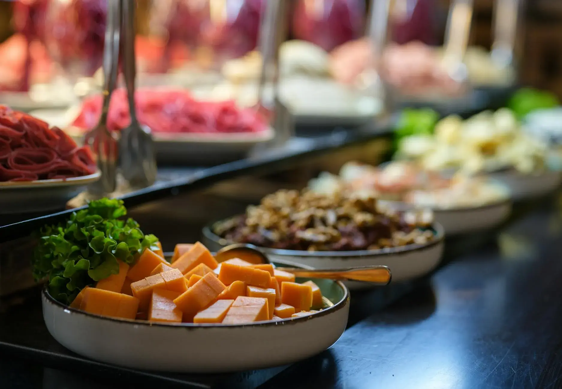 Et bredt udsnit af en vegetarisk buffet med friske råvarer som ost, salat og nødder i keramiske skåle. Stemningen understreger et sundt og indbydende måltid.