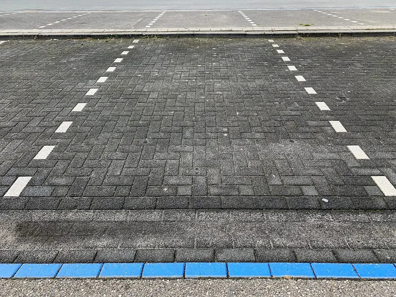 Parkeringspladser i en blå parkeringszone markeret med blå brostensindlæg. Billedet viser tydelige afmærkninger på belægningen.
