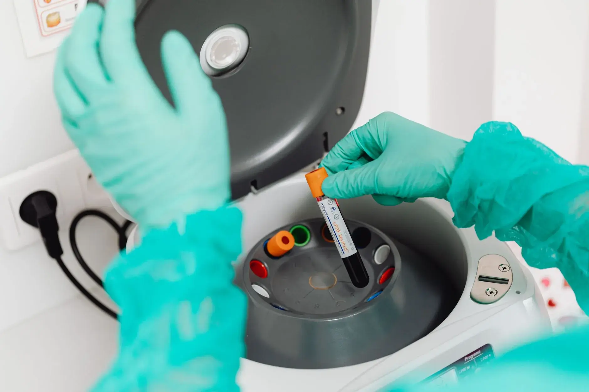 En laborant i handsker betjener en centrifuge i et moderne laboratorium. Billedet illustrerer medicinsk forskning og diagnostik.