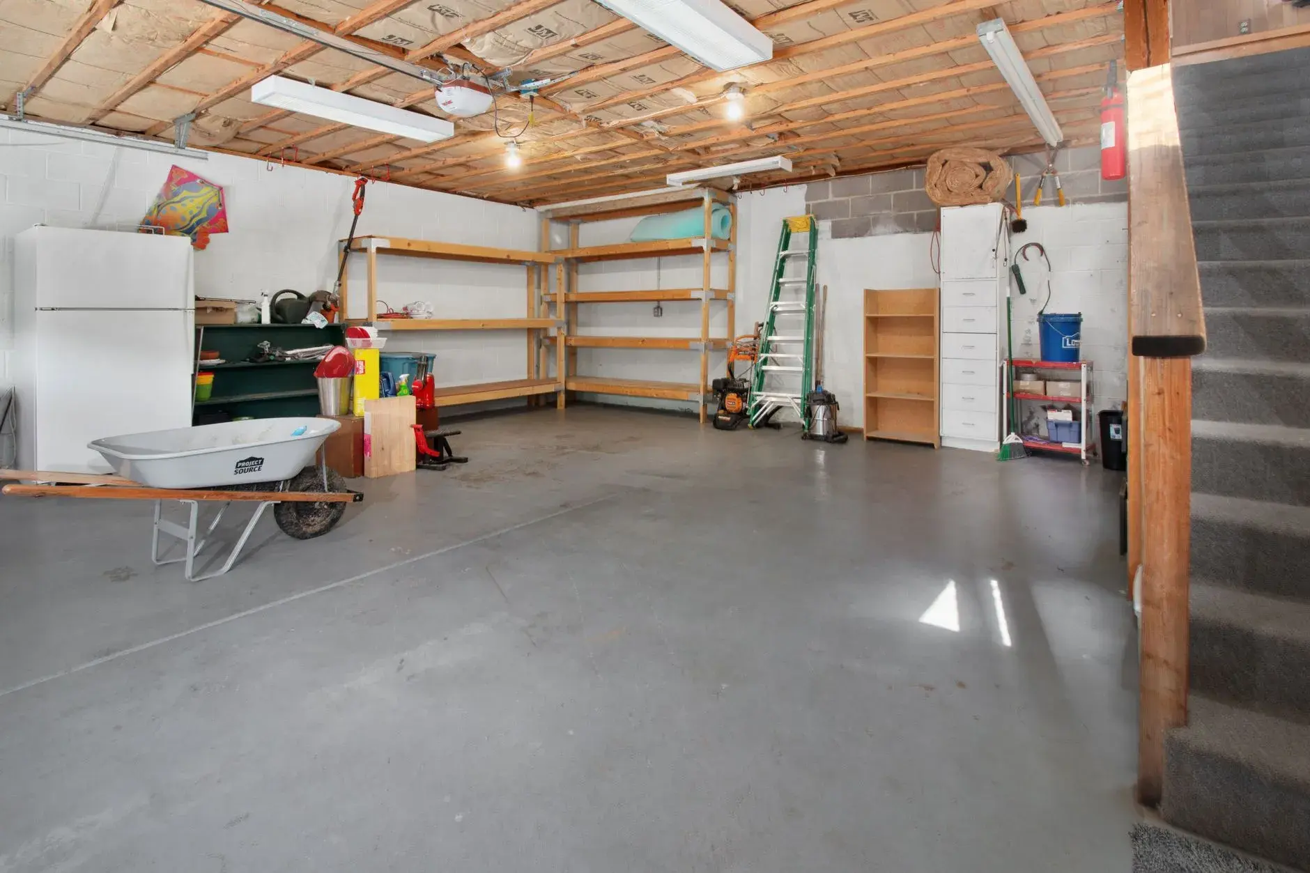 En rummelig garage med hylder til opbevaring, værktøj og en trillebør. Billedet illustrerer praktisk organisering og funktionelle hjemmeløsninger.