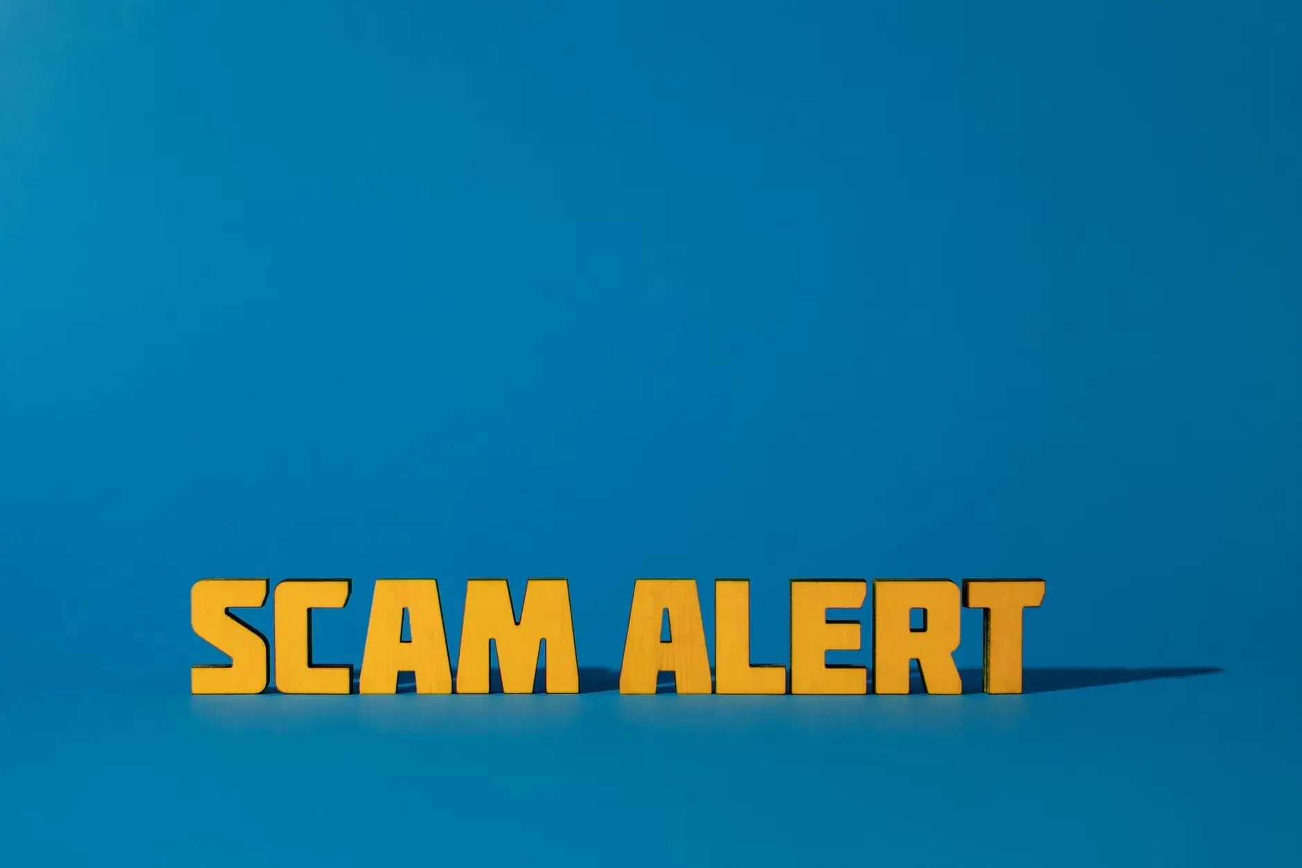 Et billede med gul tekst 'Scam Alert' på en blå baggrund, der advare mod svindel og bedrageri.