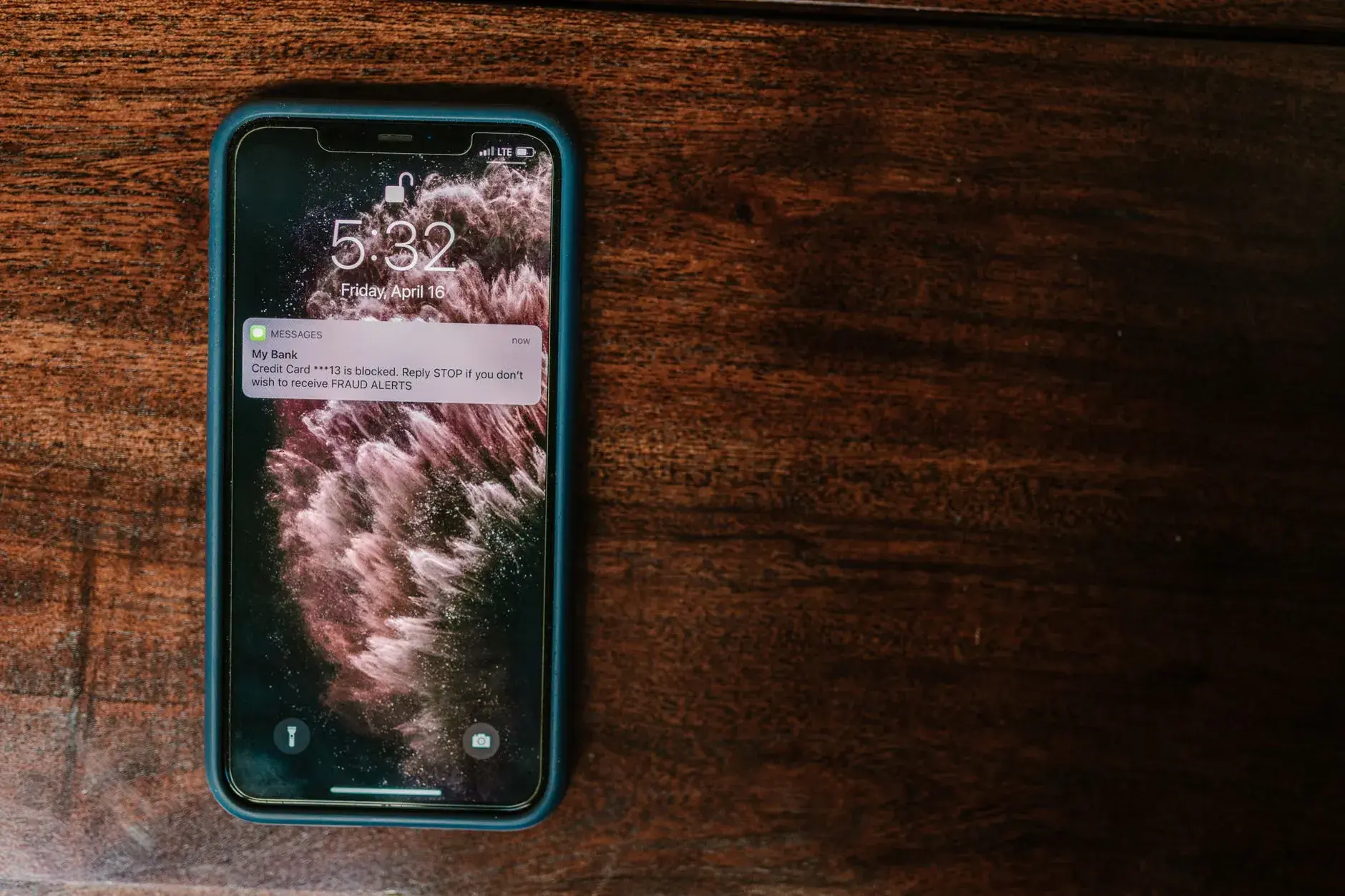 A close-up shot of a smartphone displaying a bank alert message on a wooden surface.