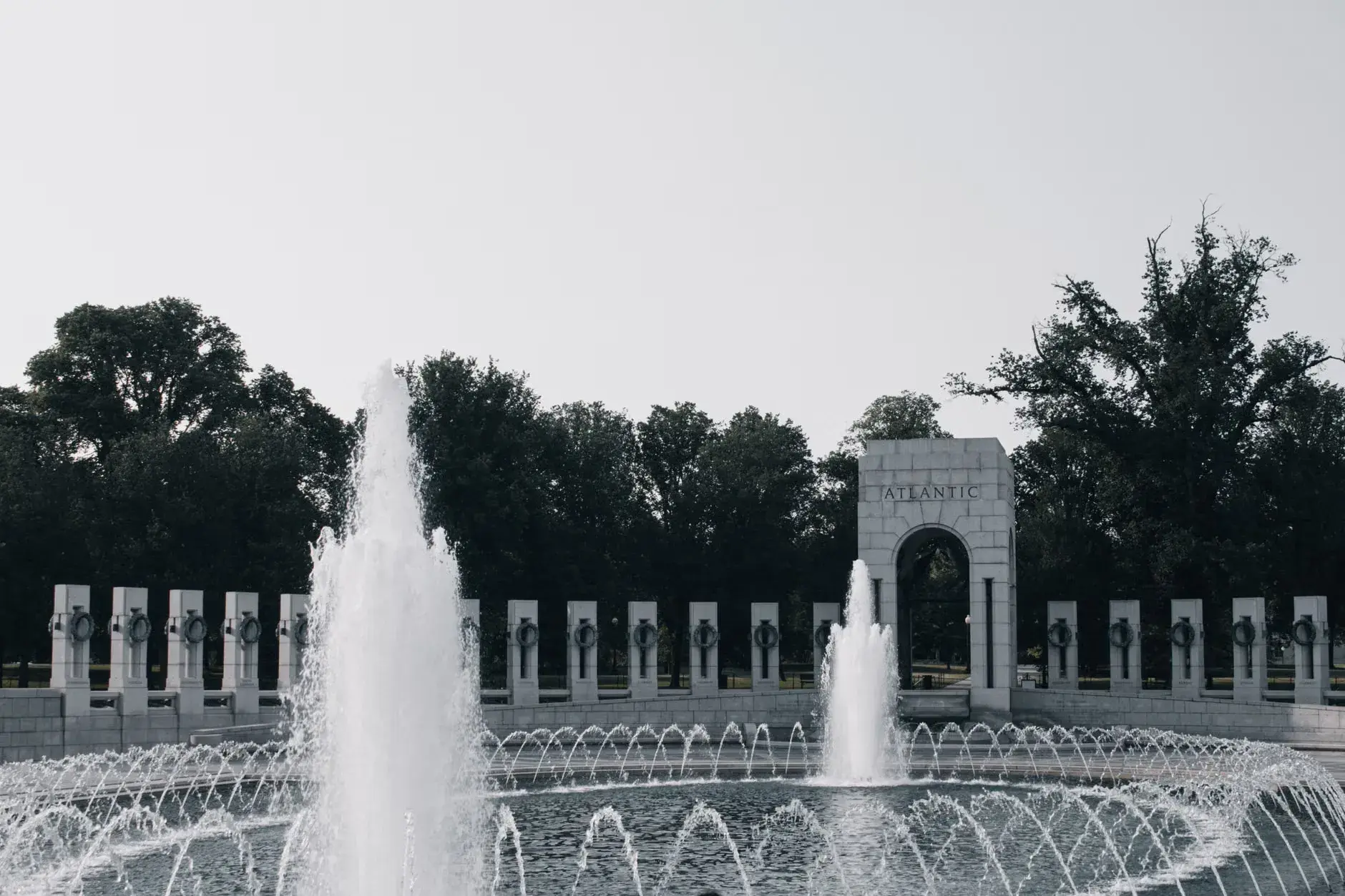En fredfyldt scene fra National World War II Memorial i Washington D.C., hvor man ser Atlantic entrance og fountains. Billedet udstråler ro og kontemplation.
