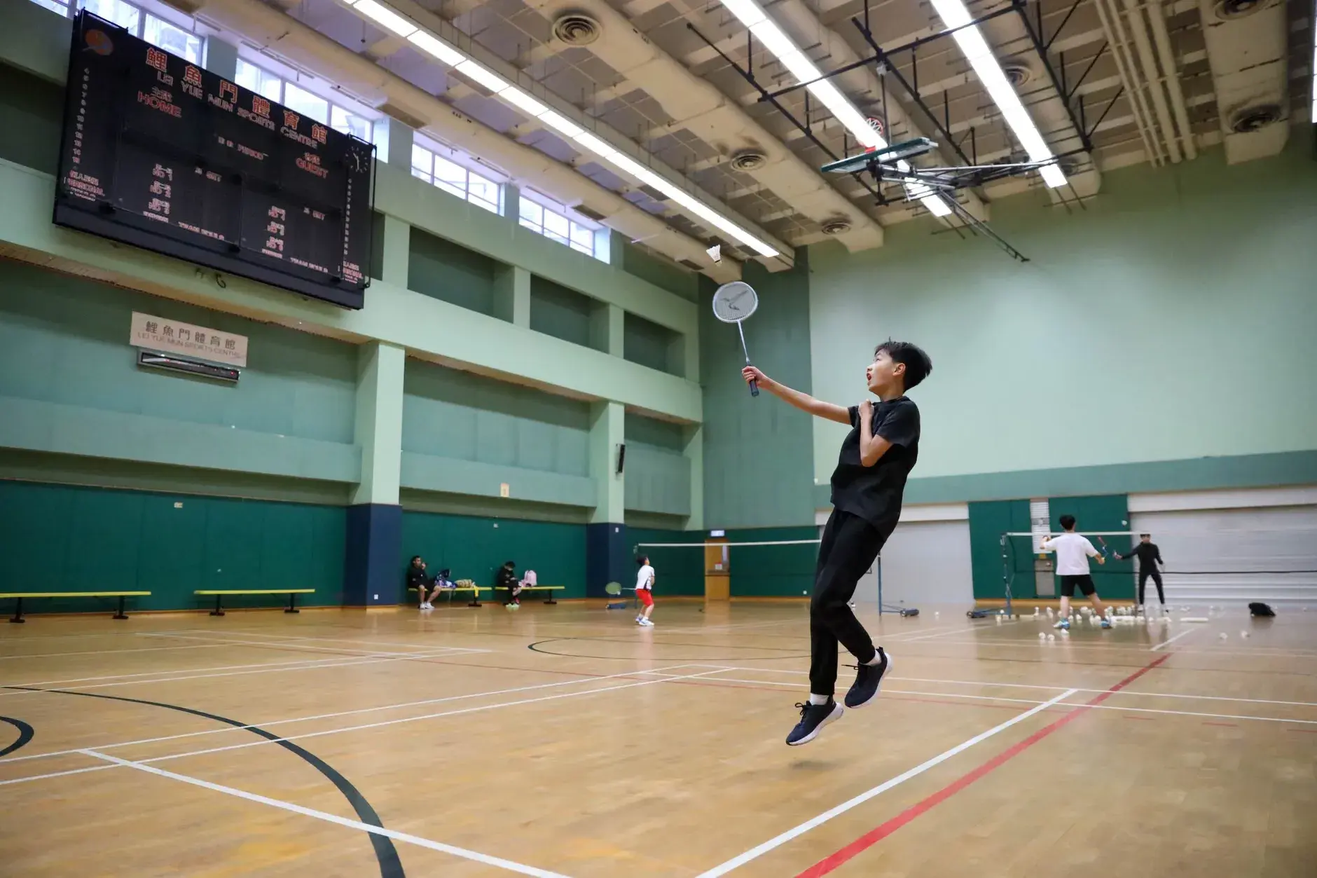 Sort-hvidt billede af en intens badmintonkamp indendørs med spillere og tilskuere. Kampen foregår i en stor hal med mange tilskuere.
