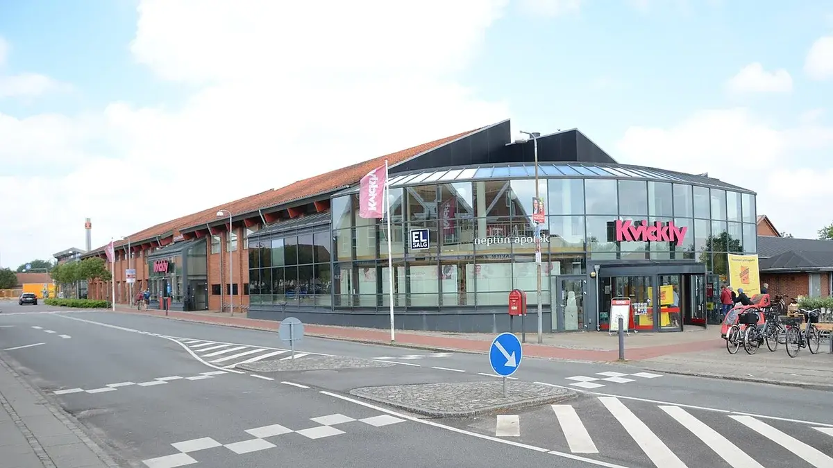 Exterior of a Kvickly supermarket with glass walls, brick sections, and bicycles parked outside.