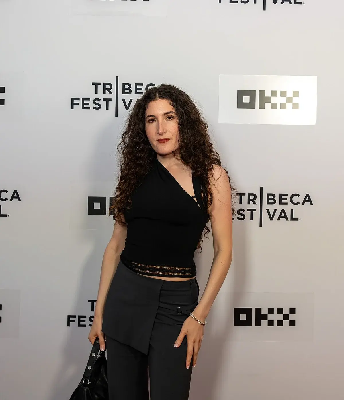 Kate Berlant posing at Tribeca Festival in front of a branded backdrop.