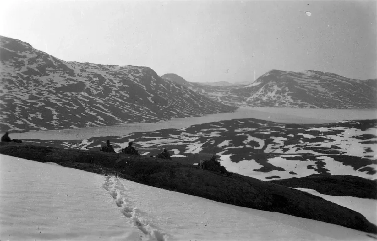 people sitting on rocky ridge overlooking snowy mountains and lake