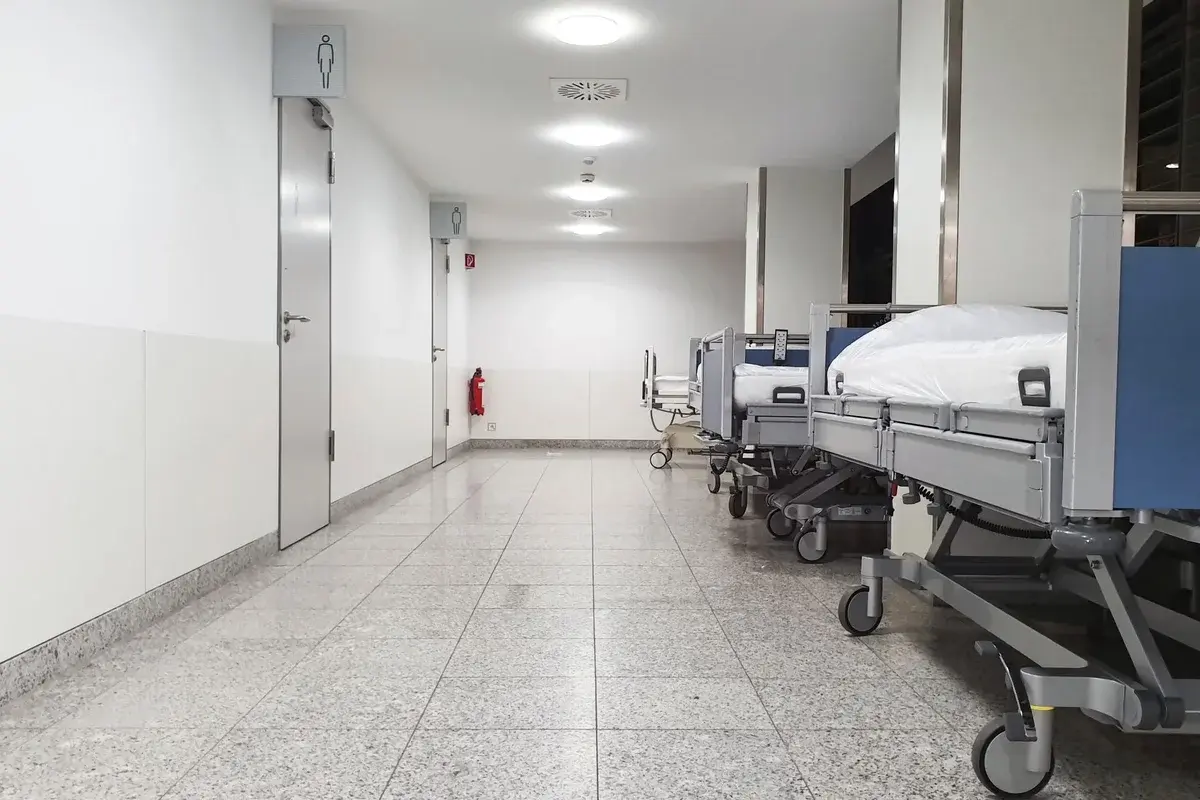 Empty hospital corridor with several beds lined up on the right side.
