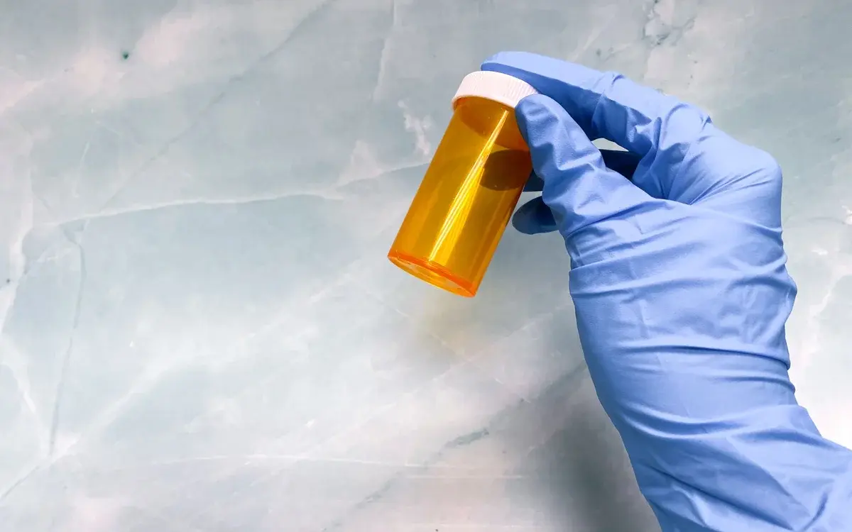A gloved hand holding an empty orange pill bottle.