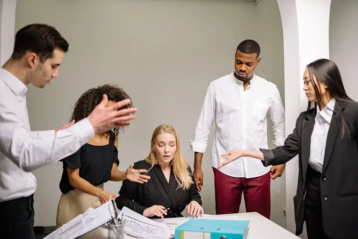 Diverse colleagues arguing or discussing intensely around a seated woman in an office.