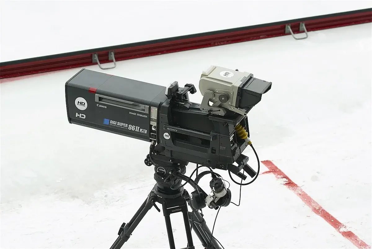 A Sony television camera with a large Canon lens on a tripod on an ice rink.