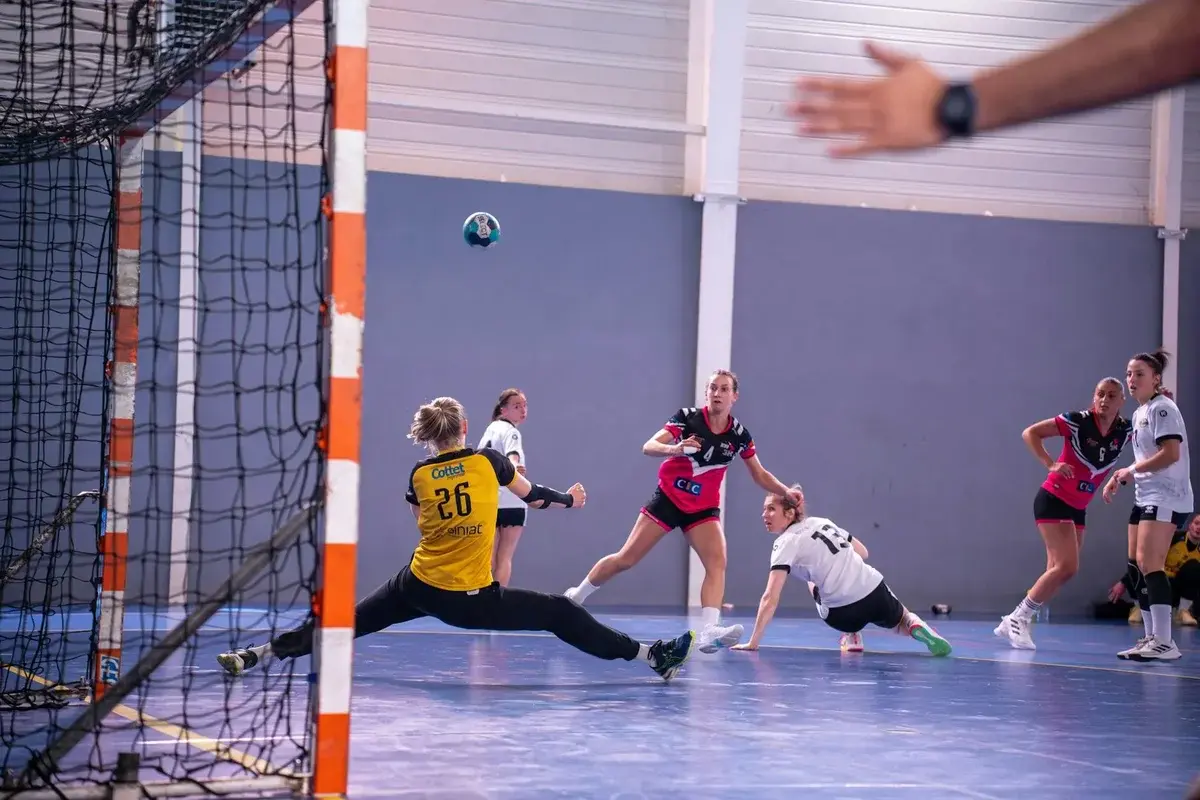 Women playing handball with goalkeeper diving to block ball