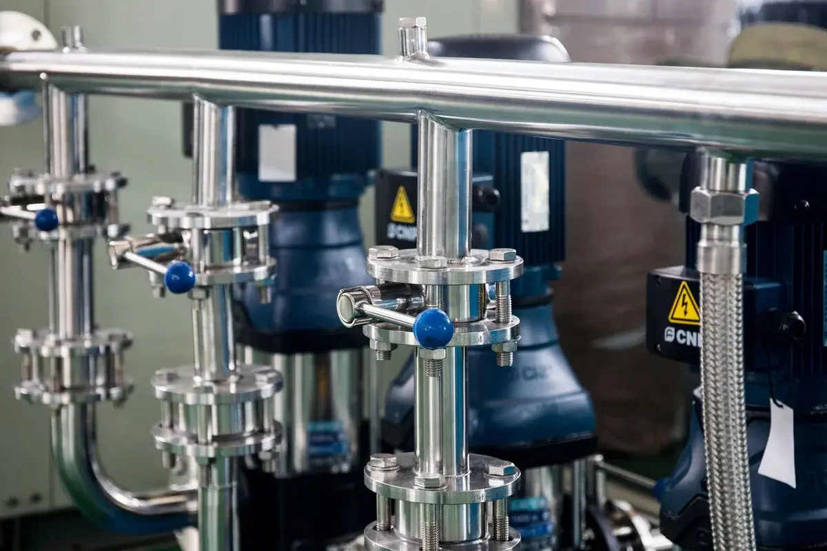 Close-up of shiny metal industrial piping and machinery inside a factory.