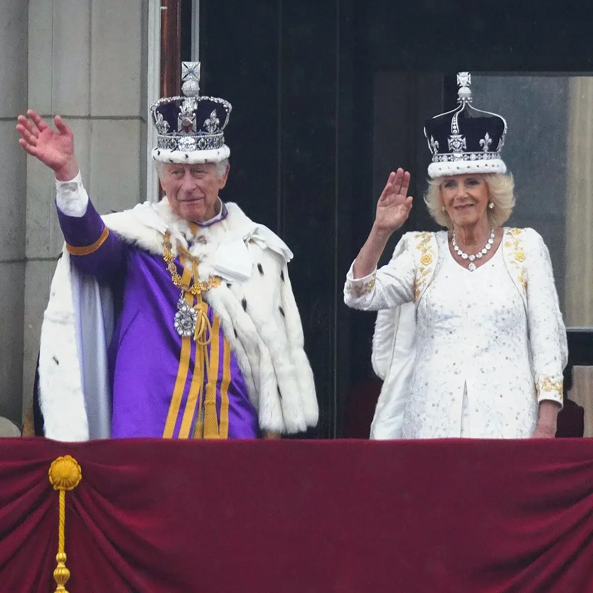 King Charles III and Queen Camilla in coronation attire waving from balcony