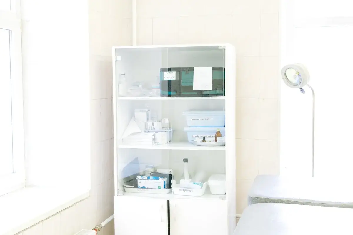 white medical cabinet with supplies next to examination table