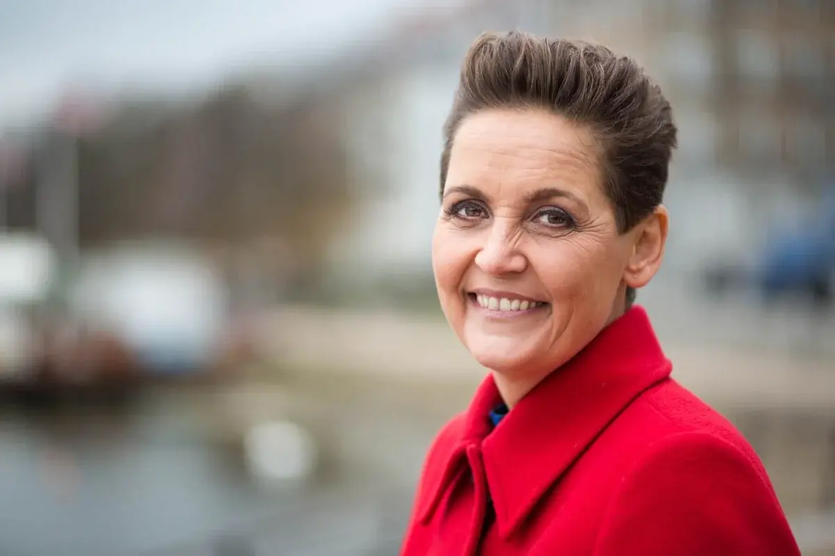 Portrait of Pia Olsen Dyhr smiling outdoors, wearing a red coat