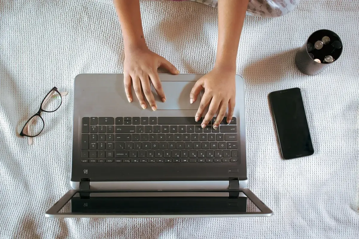 Top-down view of a laptop with hands typing, plus glasses and a smartphone.