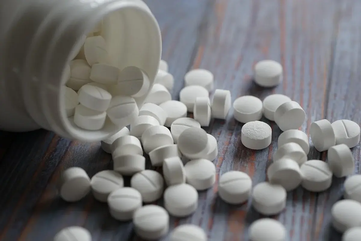 White pills spilled from a container onto a wooden surface
