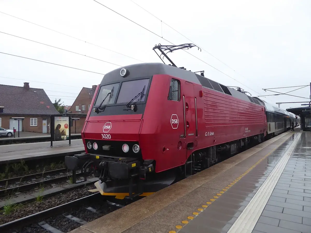 A red electric locomotive at a Danish train station platform.