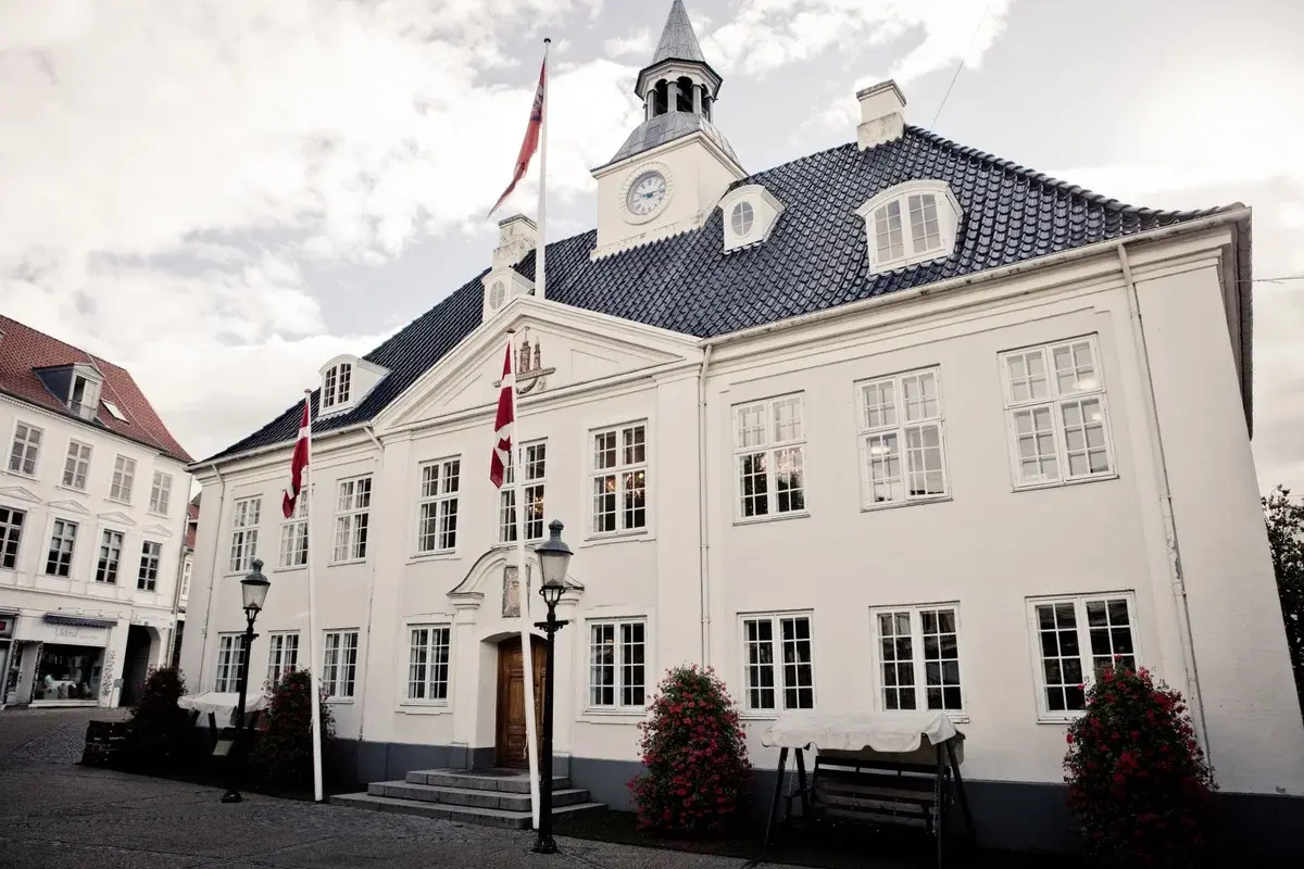 White historic town hall building with Danish flags in a town square.
