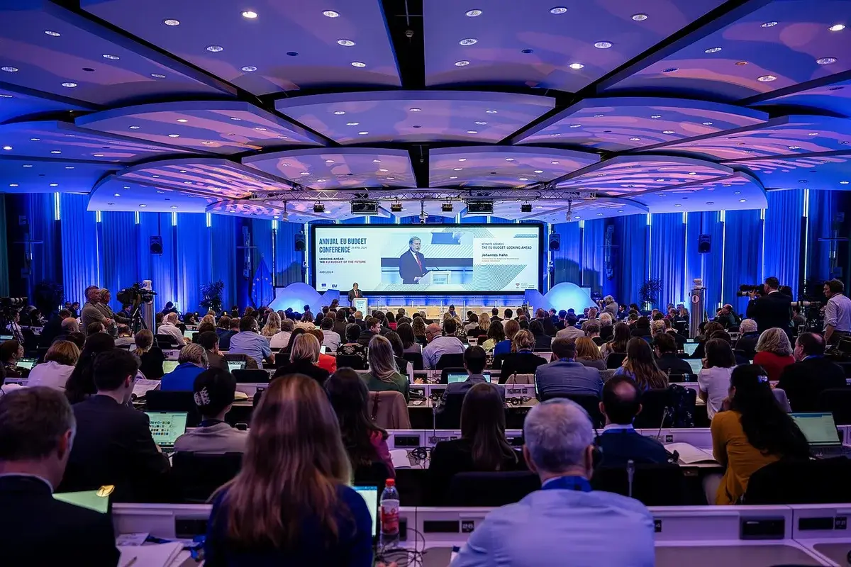 Wide shot of attendees in a conference hall watching a speaker on stage at an EU budget conference.
