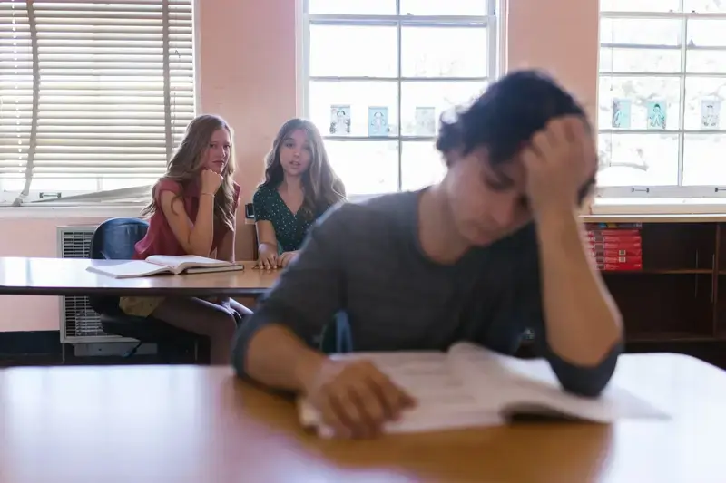 Distressed teenager with two girls whispering in classroom