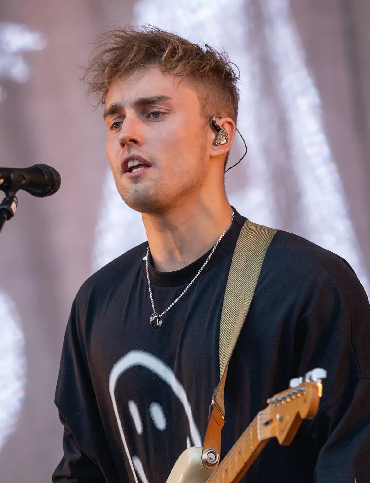 Close-up of Sam Fender performing on stage with a microphone and guitar.