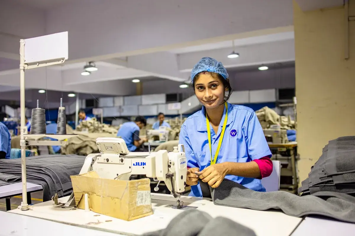 A woman sewing fabric at a machine in a garment factory.