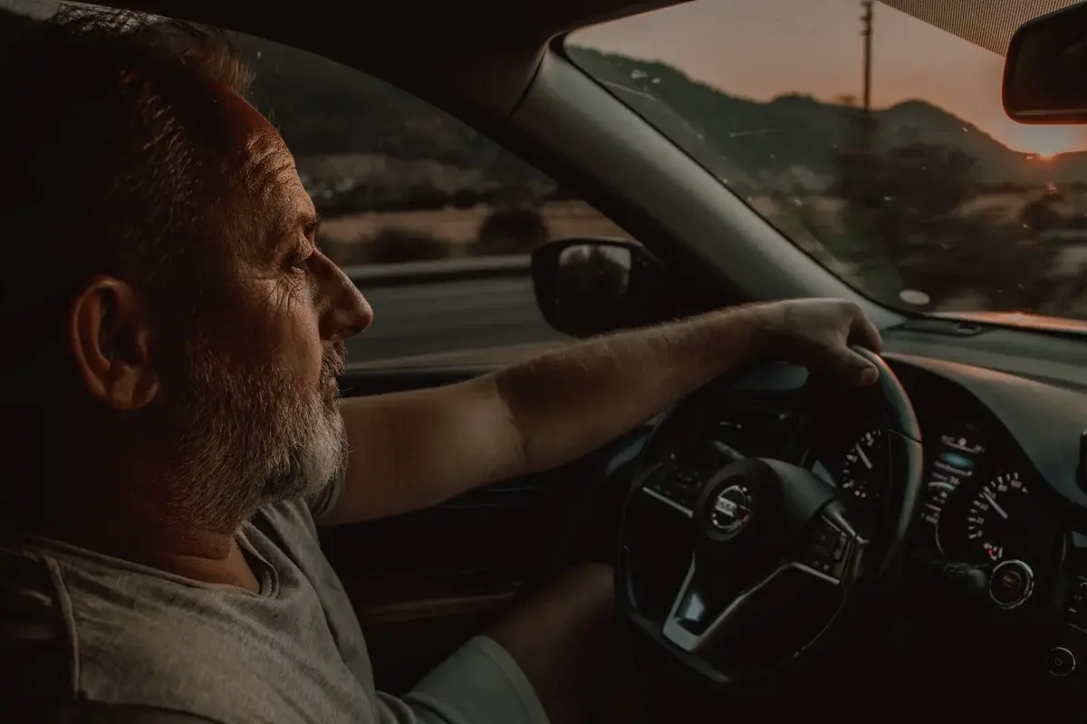 older man driving Nissan at sunset