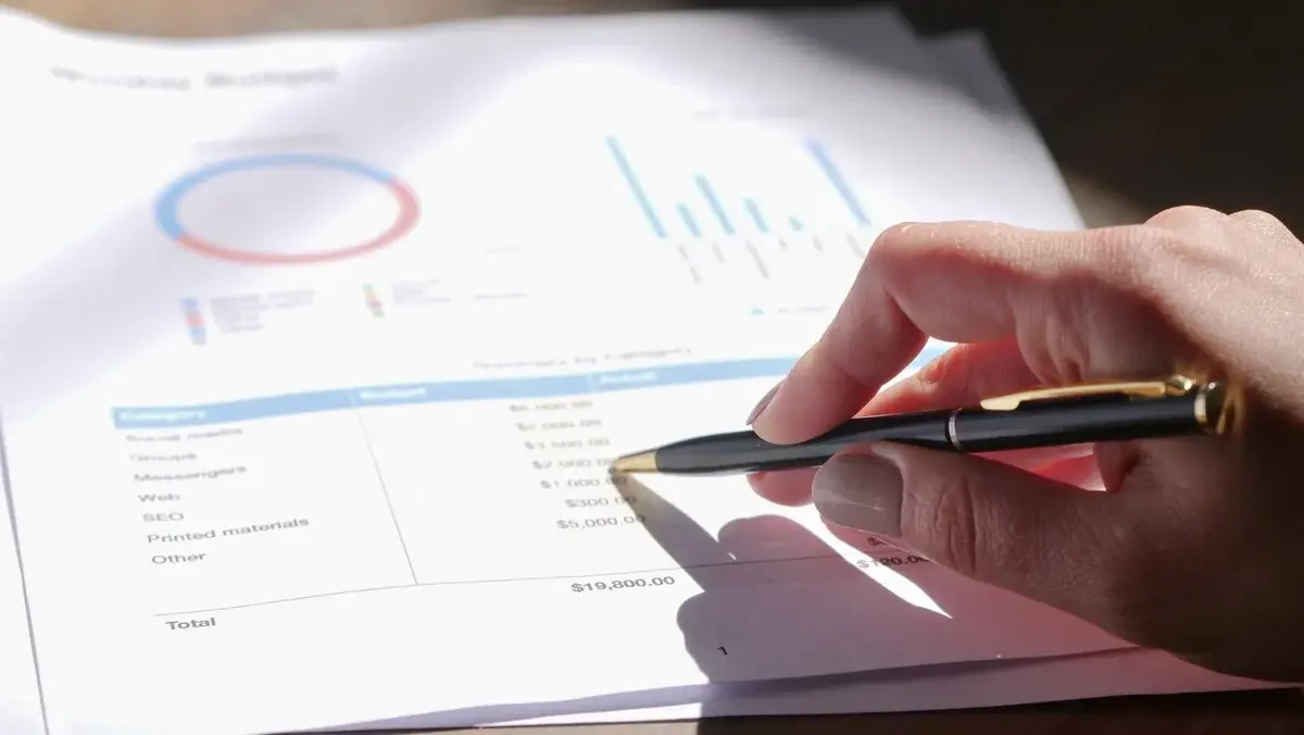 Hand with pen pointing at budget document with charts